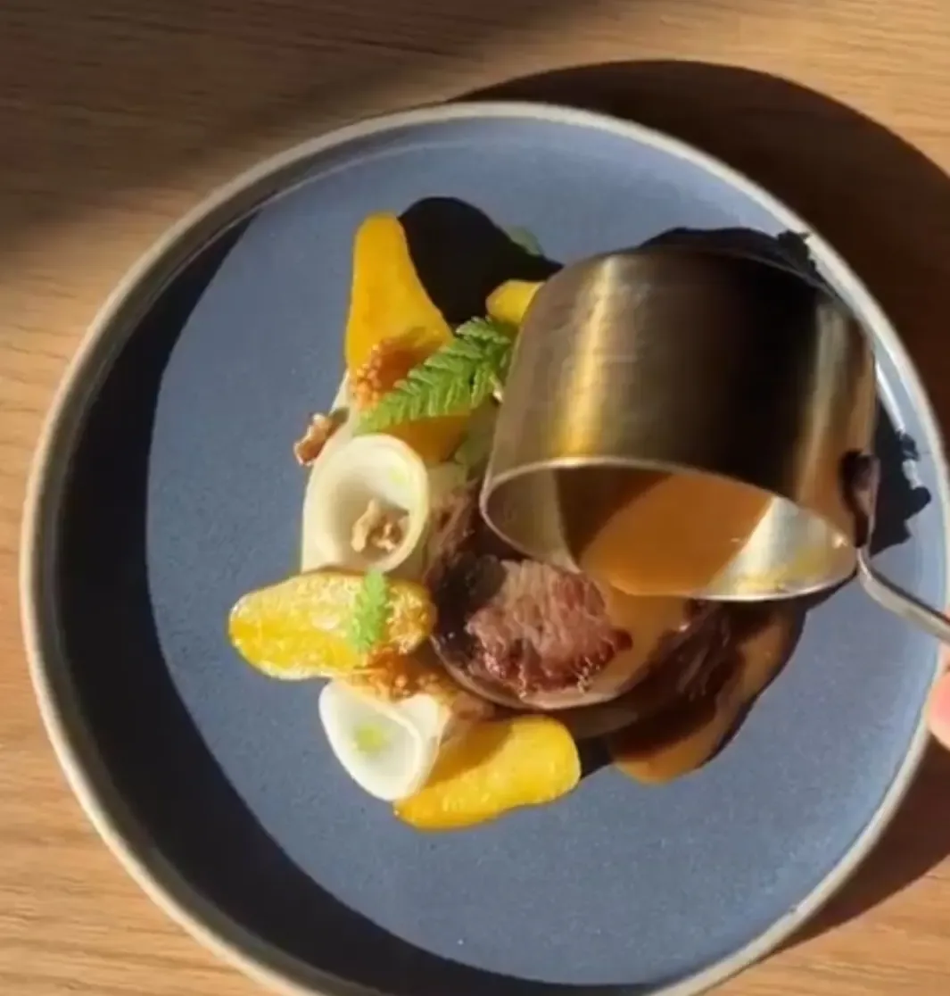 Sauce poured from a brass pot over a plate in hard sunlight