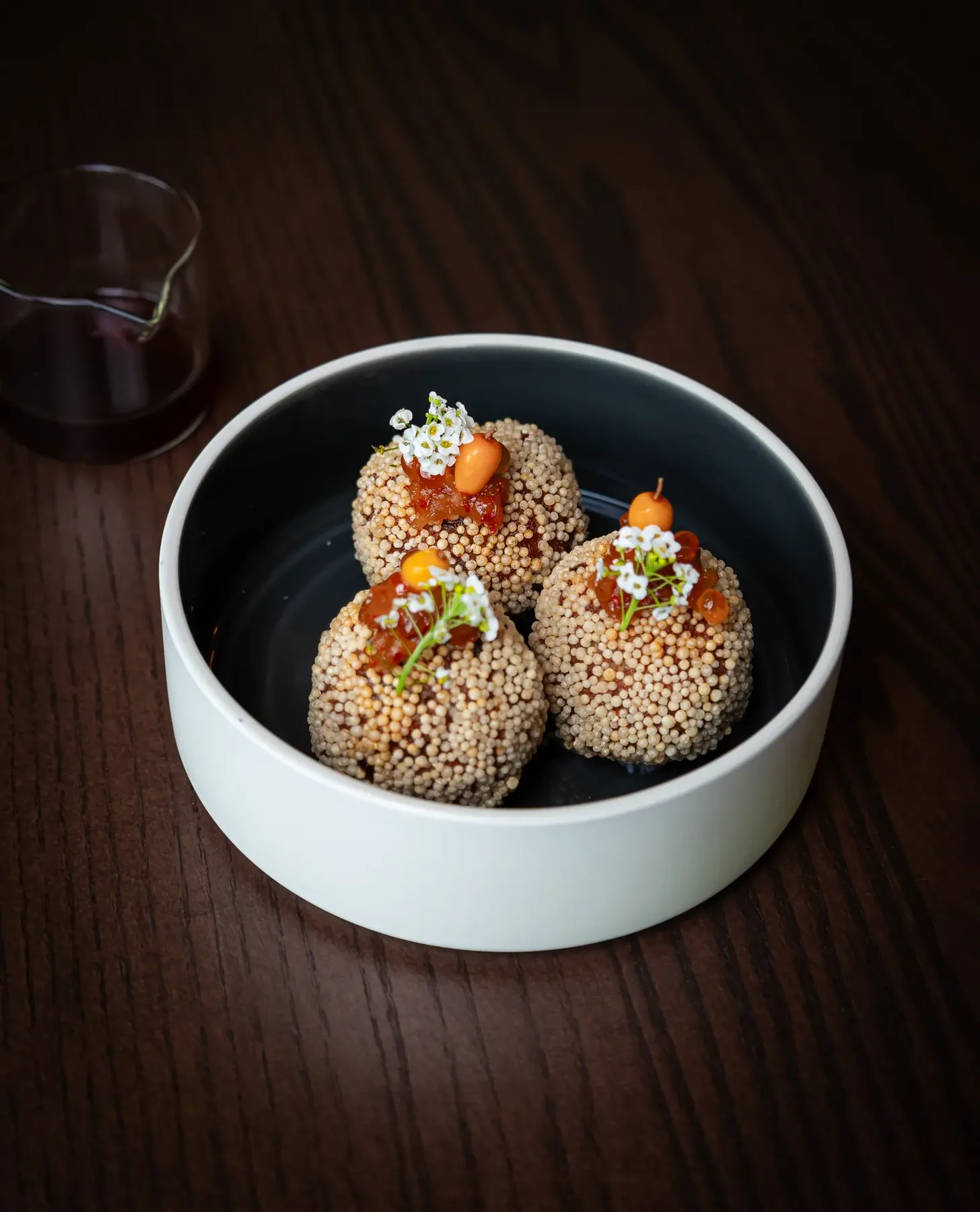 Three crisp rice balls in a white bowl on dark wood