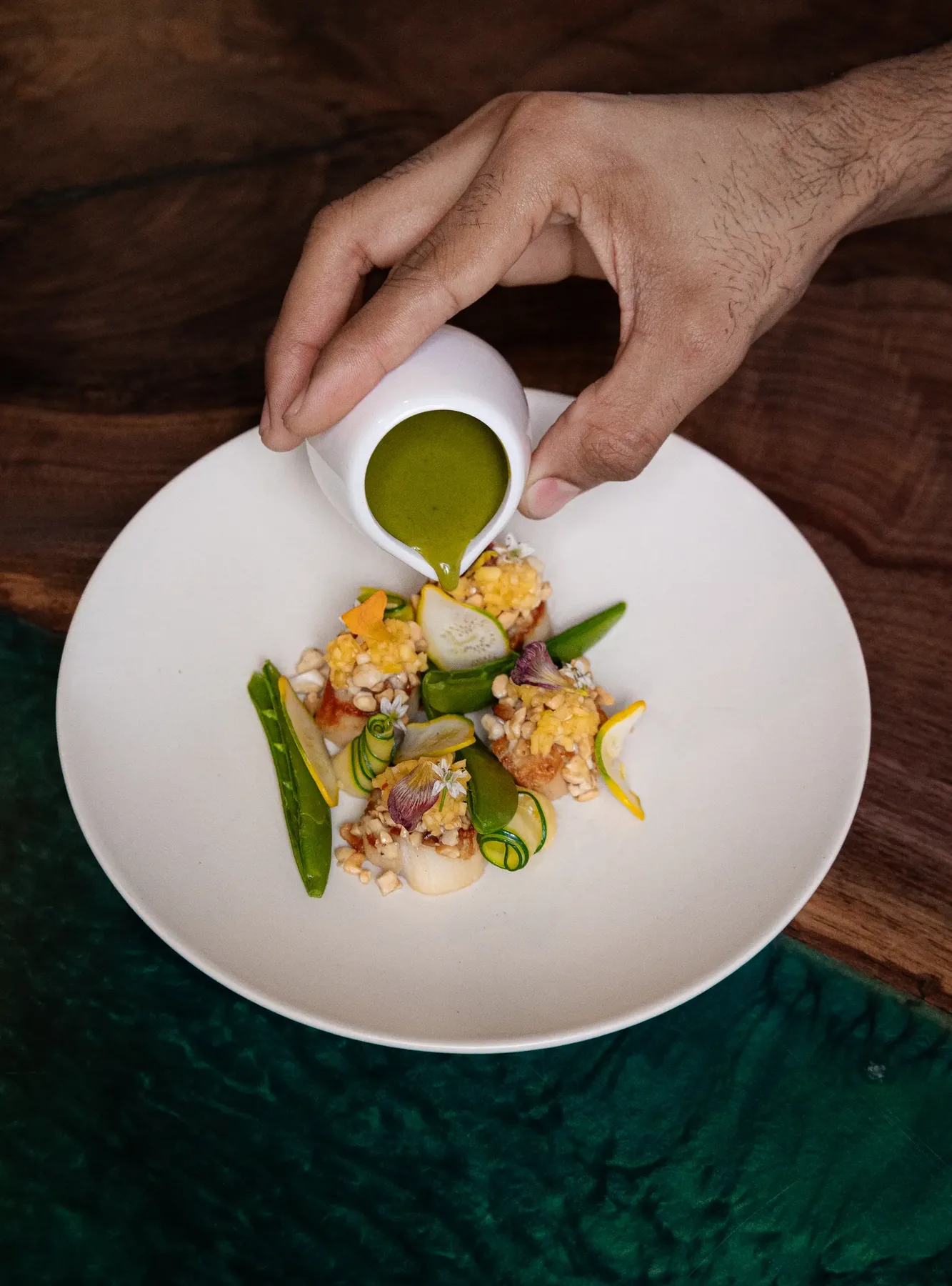 Green sauce poured from a small jug onto a plate on green velvet